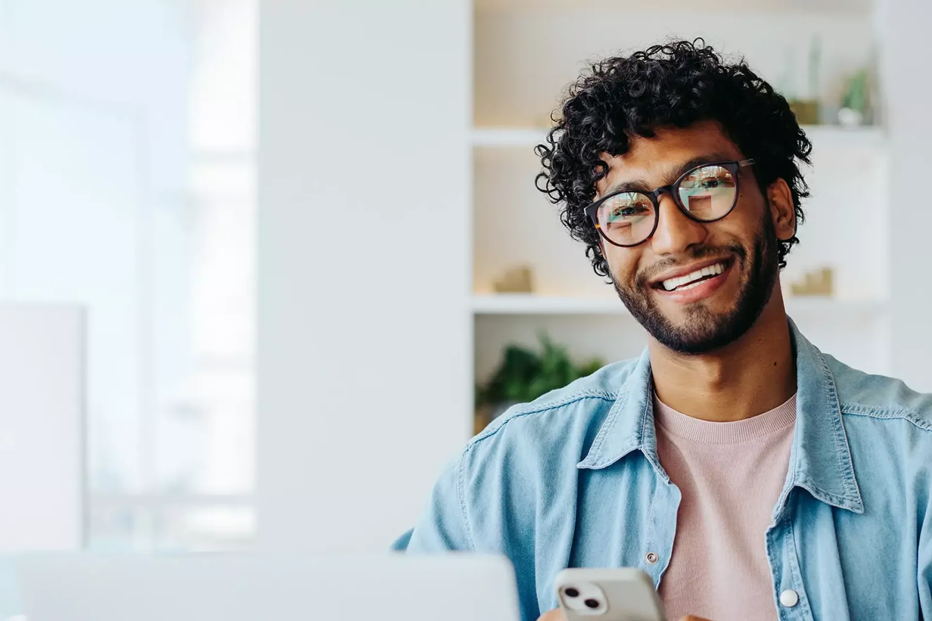 Een lachende persoon met een bril, die een smartphone vasthoudt.